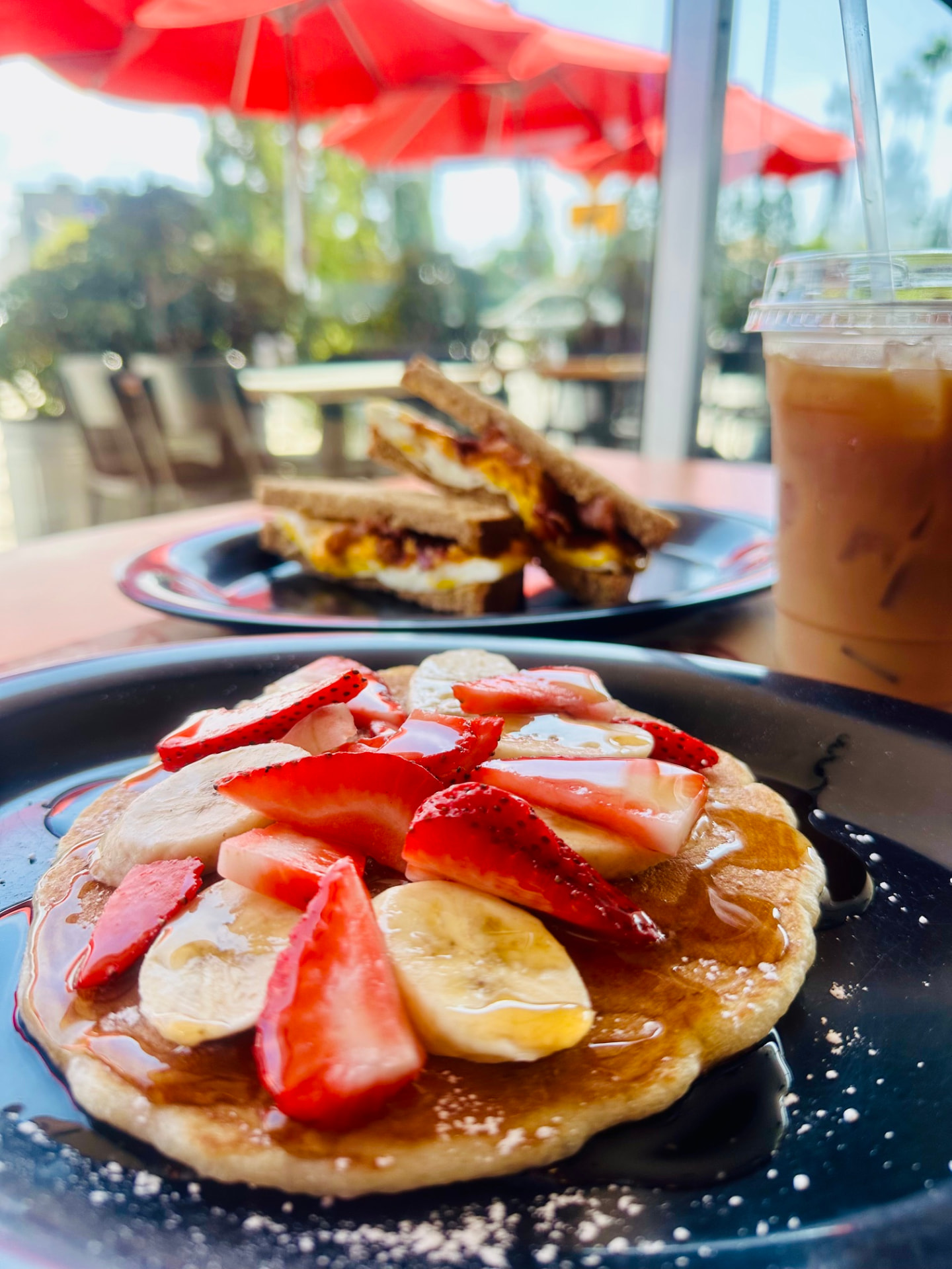 An iced latte beside pancakes and a breakfast sandwich at Rooster Cafe